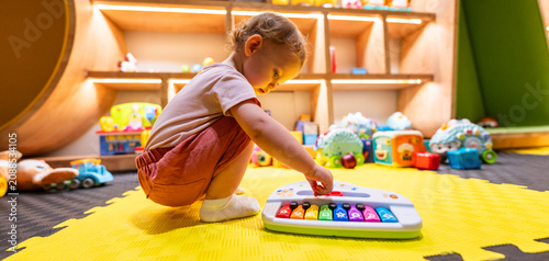 Cuadro en lienzo Toddler playing with a colorful toy piano in a bright indoor playroom