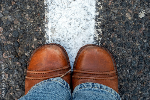 Reaching a crossroads having to decide about past, now and future symbolized by two feet and shoes standing on two different colors on pathway from above