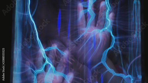 Fotografie Hand touching plasma ball, creating blue electrical energy streams and static el