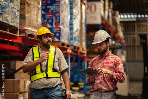 Warehouse worker and factory manager using a digital tablet to check barcodes and inspect stock inventory in an industrial logistics facility