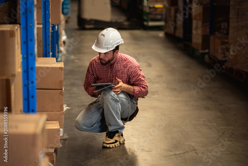 Warehouse worker and factory manager using a digital tablet to check barcodes and inspect stock inventory in an industrial logistics facility