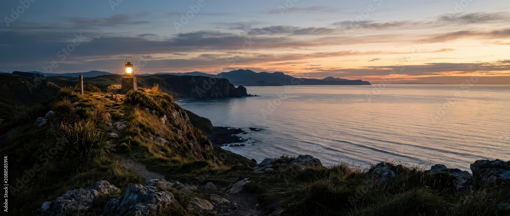 Fototapeta premium Glowing vintage lantern on a coastal cliff at twilight overlooking the sea