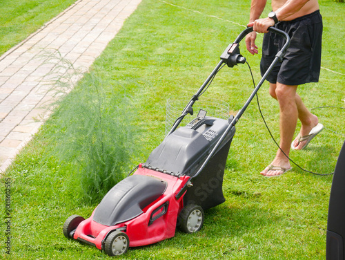 Man pushing lawn mower on green grass. Gardener cutting lawn in backyard. Professional landscaping equipment for home yard maintenance. Summer house chores and yardwork activity concept.