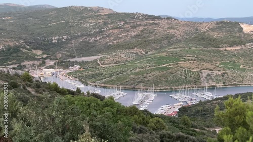 View of boats in a marina surrounded by hills and trees on a cloudy day in a coastal area