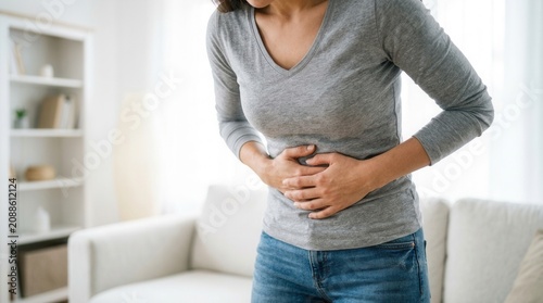 A woman suffering from acute stomach pain in a bright living room.