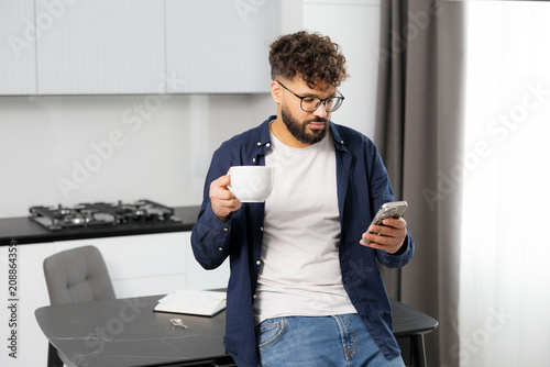 Man relaxing with phone and coffee in kitchen