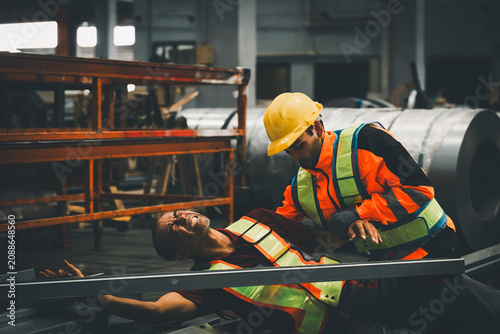 Workplace accident and industrial safety concept. Factory worker assisting injured coworker after a workplace incident in a manufacturing facility. Safety, emergency, first aid, prevention, industry