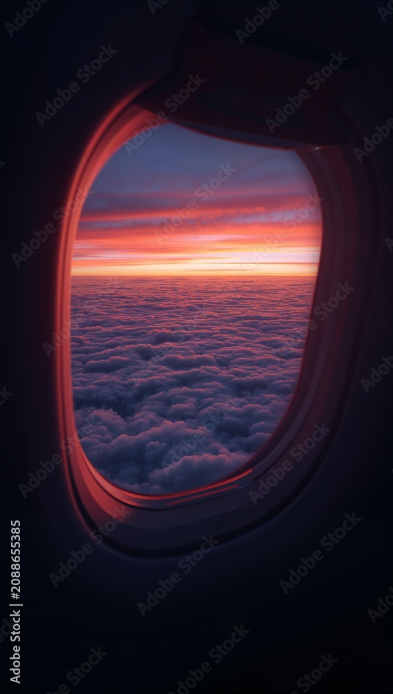 Naklejka premium Scenic view of a golden sunset over a dense layer of fluffy clouds seen through an airplane porthole window.