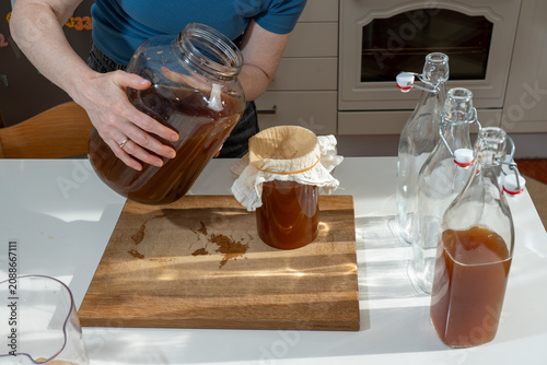 Billede på lærred Detail of the straining process as a homebrewer pours fermented tea over a natural cotton filter to ensure a smooth, yeast-free probiotic beverage