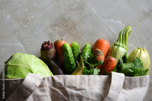 Fresh organic vegetables in reusable eco cotton bag on marble background