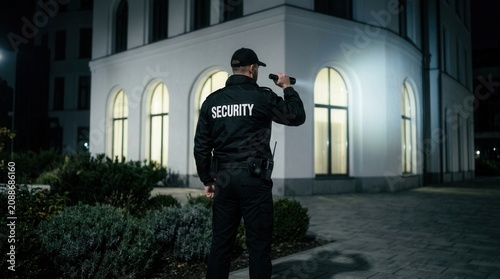 Professional security guard on patrol near a large building in the dark.