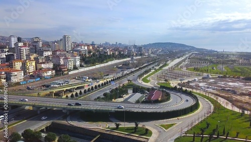 Aerial drone view of a newly constructed multi-level interchange on Maltepe coastal road with light vehicle traffic, residential buildings, green areas and partly cloudy spring sky, Istanbul, Turkey