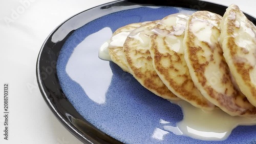 A close-up view of a stack of golden pancakes drizzled with syrup on a blue plate, showcasing the texture and color of the pancakes, emphasizing the delicious breakfast setting