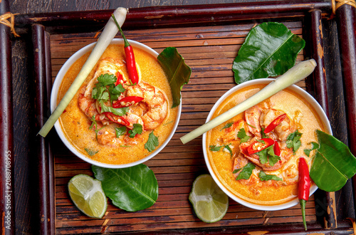 Shrimps Tom Yam Kung in grey bowl with thai spices on autentic tray top view, wooden background.