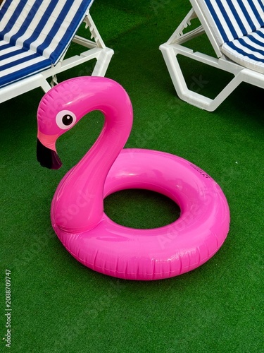 Bright pink inflatable flamingo pool float on a green grass lawn near sunbeds at a summer resort.