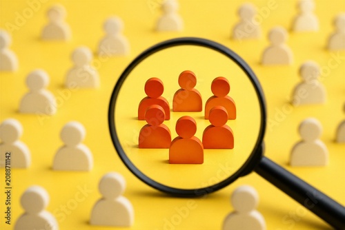 A magnifying glass shows a group of orange figures set against a larger group of white figures on a yellow background. This scene highlights the orange figures in the center.