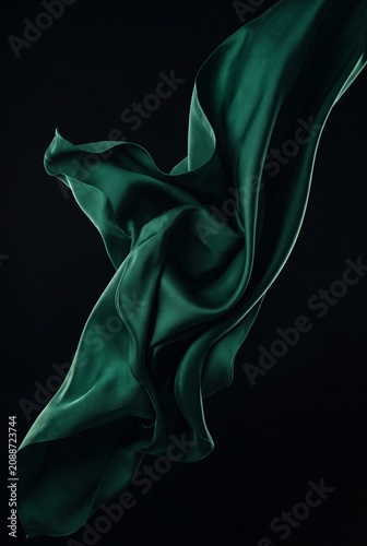 Elegant emerald green silk fabric flowing and waving against a solid black background