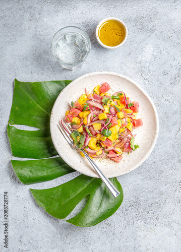 Tropical Hawaiian tahitian tuna mango salad on white plate on tropical monstera leafe