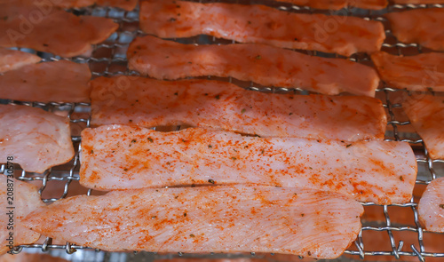 Cured pork belly strips seasoned with red paprika and spices arranged on stainless steel racks inside an industrial drying chamber.
