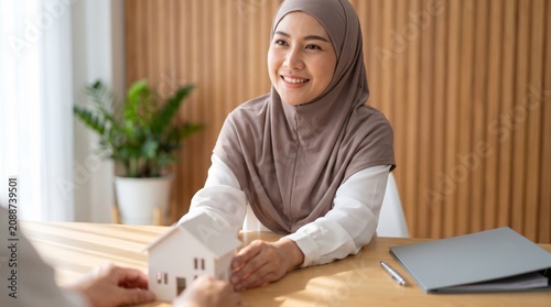 Islamic mortgage advisor in taupe headscarf presenting house model across desk