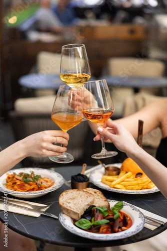 Friends toasting with wine during restaurant dinner
People clinking wine glasses over gourmet meal
Couple celebrating with wine in elegant restaurant