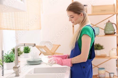 Obraz na plátně Teenage worker washing dishes near sink in kitchen, space for text