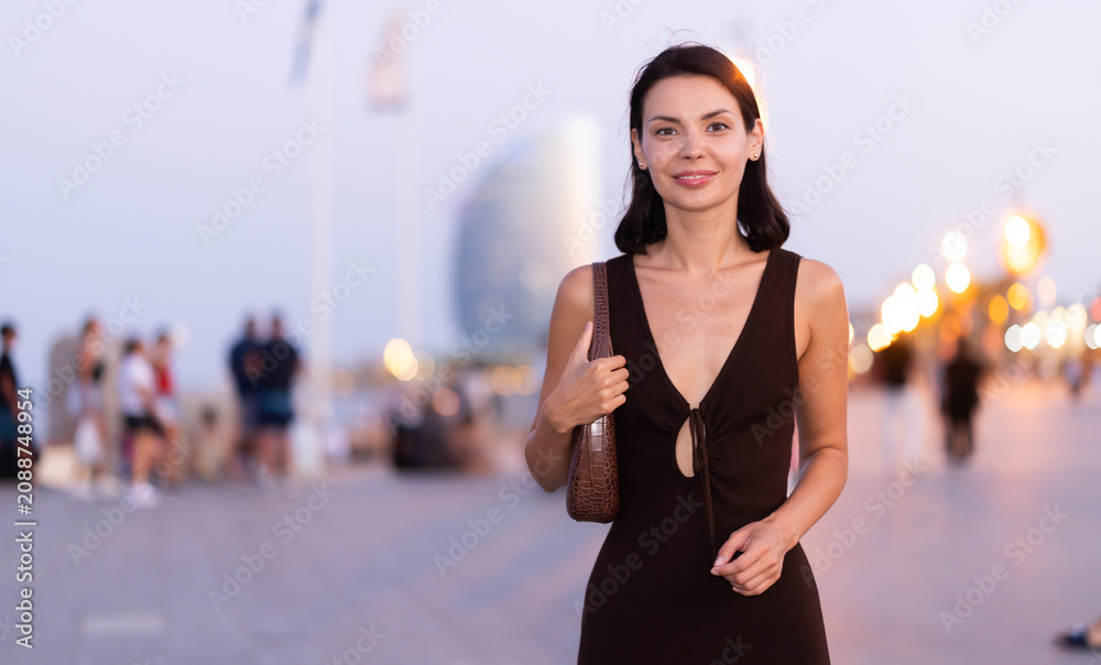 Naklejka premium Slender female brunette walks in vicinity of beach in Barceloneta, spends time in motion, walks and enjoys sunny warm day. Carefree, promenade..
