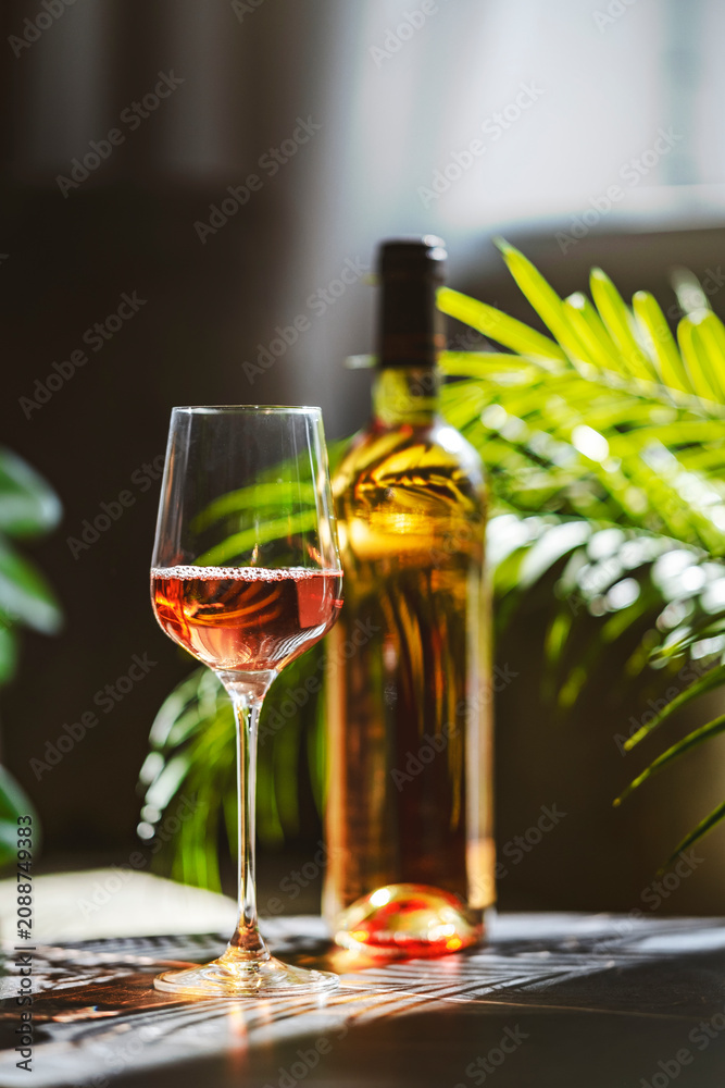 Fototapeta premium Chilled blush rose wine bottle and glass on table. Sunny summer patio relaxation and Mediterranean lifestyle outdoor dining concept.