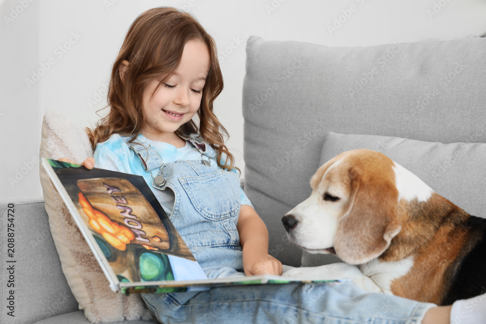 Obraz premium Cute little girl with Beagle dog reading book on sofa in living room