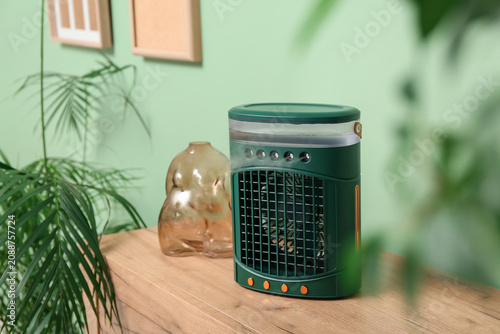 Fotografie Portable table fan with humidifier and decor on chest of drawers near green wall
