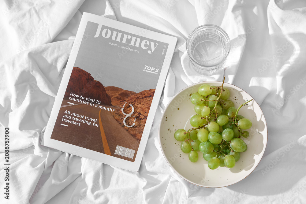 Fototapeta premium Plate with sweet ripe grapes, magazine and glass of water on white fabric background