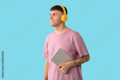 Handsome young happy man in headphones with tablet listening audiobook on blu...