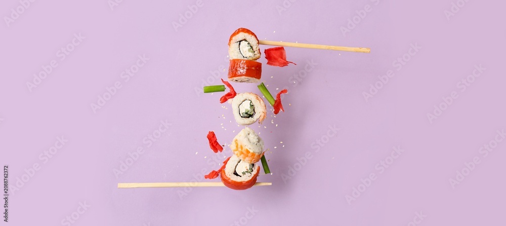 Fototapeta premium Floating sushi rolls with chopsticks on purple background