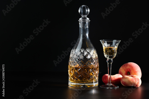 Obraz na plátně A leaded-glass carafe filled with peach liqueur and a glass are placed against a dark background