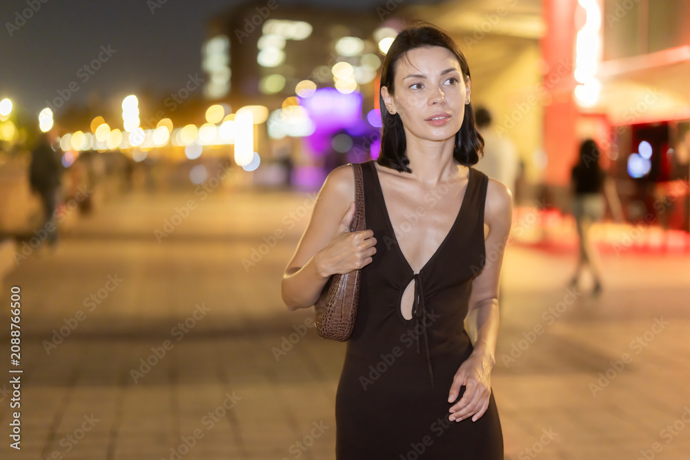 Naklejka premium Woman walks in vicinity of Passeig de Sant Joan, spend time in public urban space. Atmosphere of relaxation, idleness, entertainment. Electric street lighting, night life in big city
