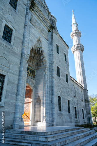 Vertical photo of a ottoman mosque entry in white marble material architecture with a minaret and a clear blue sky.