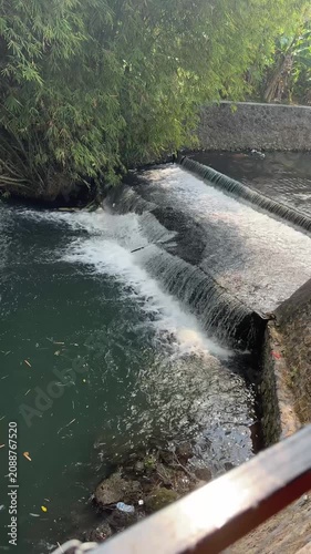 Observing a Calm Waterfall Over a Small Dam in a Lush Park