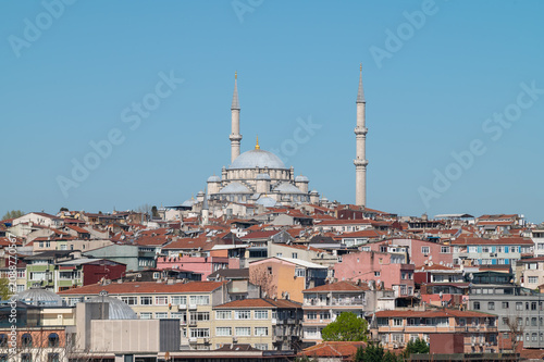 horizontal photo of a cityscape view of a ottoman mosque in a hill surrounded by buildings with a clear sky.