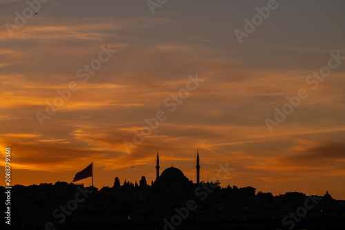 horizontal photo of a city landscape with silhouettes of a mosque in the center and other buildings in the sunset of istanbul.