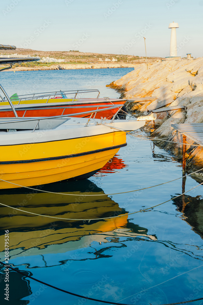 Fototapeta premium Yellow fishing boat and other small vessels are moored together at a harbor quay on a clear day.