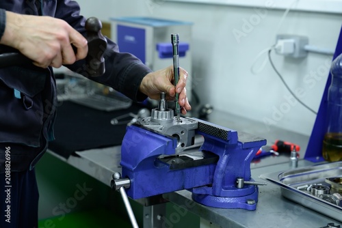 Mechanic hand using hammer and pin punch tool on high pressure diesel fuel pump fixed in vice clamp inside workshop
