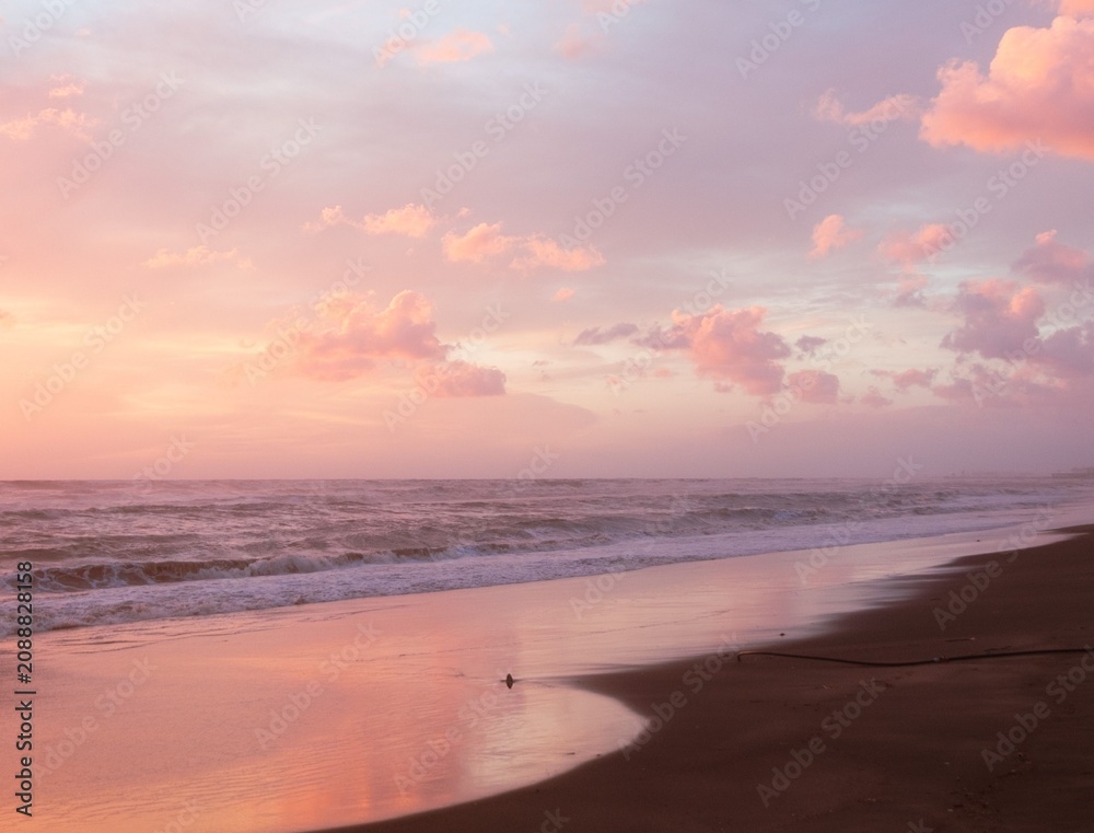 Obraz premium Peaceful beach at sunset featuring gentle ocean waves, golden light, and a colorful evening sky.