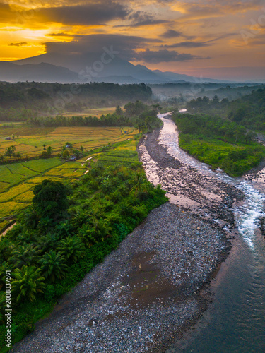 Beautiful panoramic aerial view of terraced rice fields at sunrise in Indonesia, surrounded by lush tropical greenery and palm trees