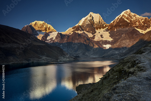 At the edge of Carhuacocha lagoon, the great triumvirate of the Cordillera Huayhuash reveals itself in a reflection of almost unbearable clarity. Siula Grande, Yerupajá and Jirishanca rise in savage, 