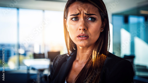 Anxious businesswoman with furrowed brow and wide eyes in a modern office, facing concern, perfect for stress management, corporate communication and mental health awareness campaigns
