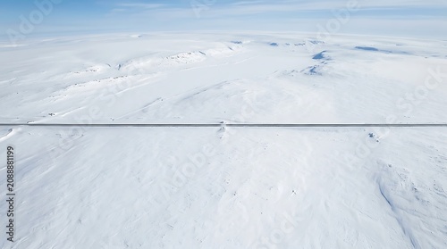 Aerial view of train track winding through vast snowy landscape under clear blue sky