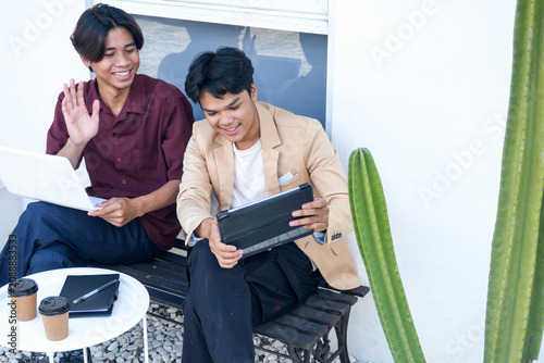 Two Smiling Asian Man Working Together Outside with Laptop and Tablet