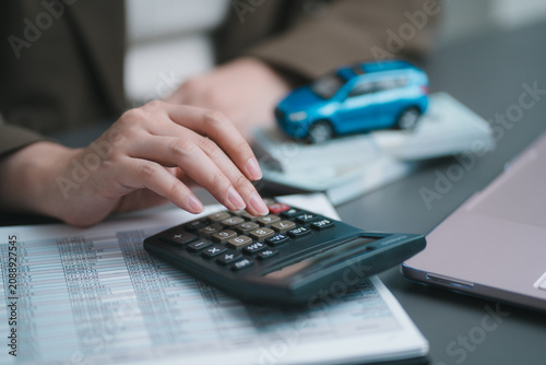 Accountant hand using calculator to check finance document report. Business woman calculating car loan cost, automotive insurance premium and auto tax budget at office desk