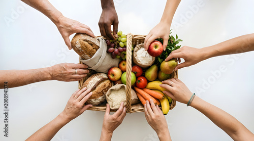 Top View of Diverse Hands Reaching Into a Large Wicker Basket Filled with Fresh Produce and Bread as Community sharing