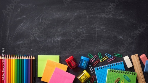 Flat lay composition of colorful school stationery, notebooks, and pencils arranged on a rustic dark chalkboard surface with copy space for text.